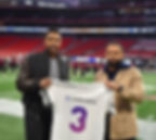 Two people holding up a Lockerverse jersey in a stadium.